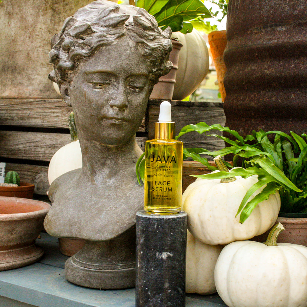 Face Serum next to statue of woman's face in a  greenhouse setting